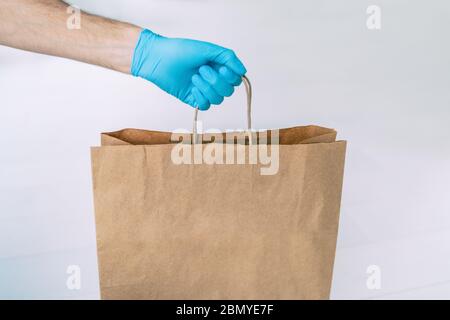 Home delivery during COVID-19 quarantine from coronavirus self isolation lockdown. Grocery store shopping delivery man giving paper bag wearing blue Stock Photo