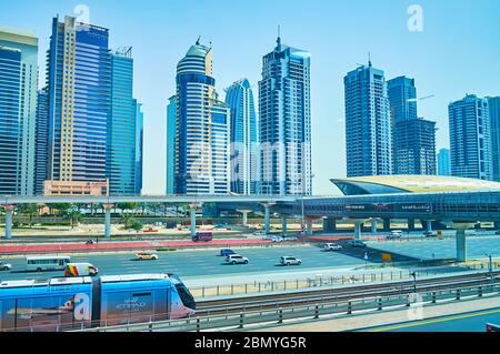 DUBAI, UAE - MARCH 2, 2020: The riding tram, Sheikh Zayed road with fast traffic, skywalk and the pavilion of metro station in front of Jumeirah Lake Stock Photo