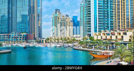 DUBAI, UAE - MARCH 2, 2020: Panorama of Dubai Marina with moored yachts, wooden dhow boats and lush palm trees, growing along Marina Walk, on March 2 Stock Photo