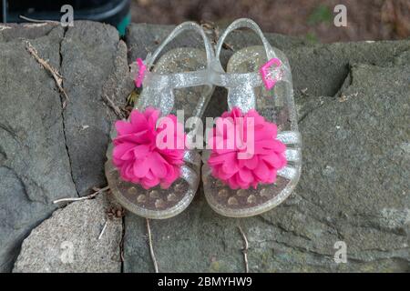 a close up view of a small pair of plastic clear girls shoes with a pretty pink flower on the front Stock Photo