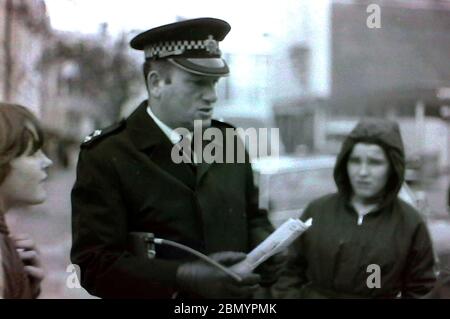 A senior police officer with a radio under his arm talks to young people in the street in Manchester, uk, in the 1970's Stock Photo