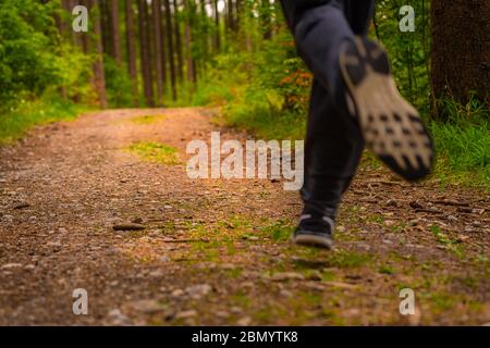 Jogging feet of a running man from low perspective in a green forest at springtime. Dynamic photo of a popular human activity to increase somebodys Stock Photo