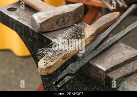 Puyallup, Washington, USA.   Blacksmith hammer, tongs and brush resting on an anvil. Stock Photo