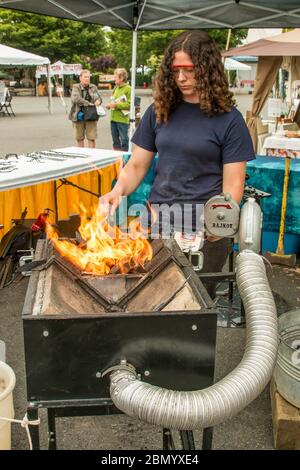 Puyallup, Washington, USA.   Young woman blacksmith hand cranking a blower on a portable forge. Stock Photo
