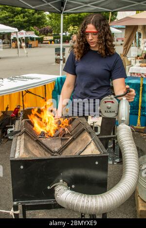 Puyallup, Washington, USA.   Young woman blacksmith hand cranking a blower on a portable forge. Stock Photo