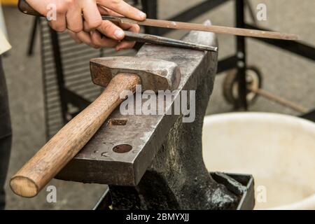 Female blacksmith picking up a file and chisel and  Puyallup, Washington, USA. Stock Photo