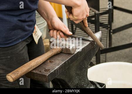 Puyallup, Washington, USA.   Female blacksmith filing a hot iron piece. Stock Photo