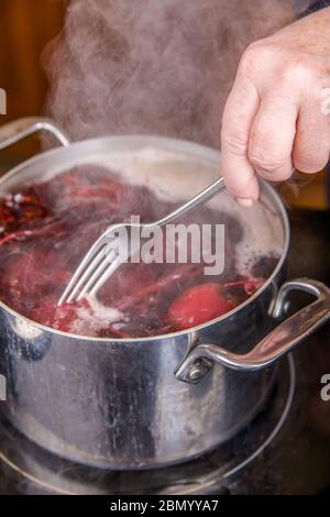 Woman testing the beets to see if they are cooked by poking them with a fork.  This is a step in the making of canned pickled beets. Stock Photo
