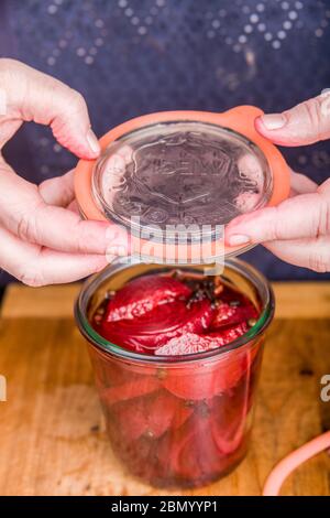 Woman placing a lid on a Weck canning jar of beets and pickling solution.  These jars are made of thick glass to withstand boiling and sterilization. Stock Photo