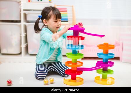 toddler girl play marble run game at gome agianst white background Stock Photo