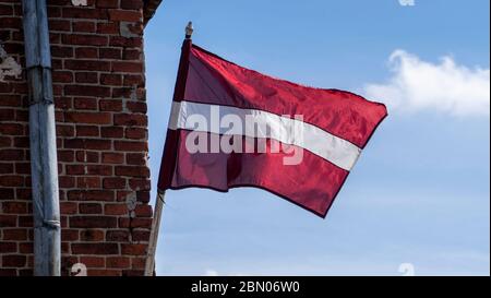 Latvian Flag on the Reddish Brick Wall  an Old Building. Background of a Wall With Old Stones. Stock Photo