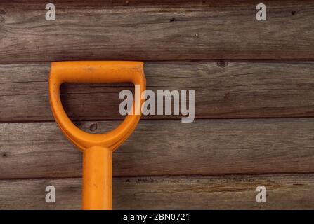 Close up orange garden tool handle on light brown wooden background on left side. Wide horizontal minimalist composition, copy space Stock Photo