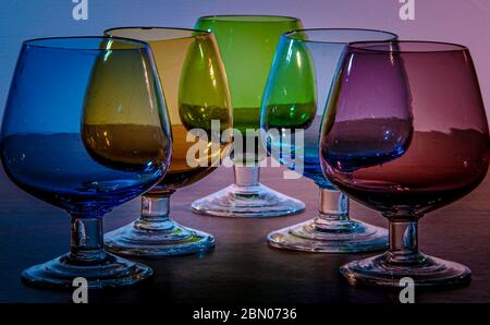 Primary coloured stained glass shot brandy liqueur sherry glasses arranged in a symmetrical fashion on a dark wooden surface Stock Photo