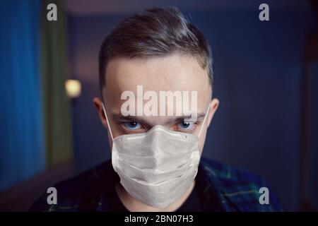 Distraught in home isolation, a young Caucasian man. The crazy look of a white male who wears a protective face mask indoors during the period of coro Stock Photo