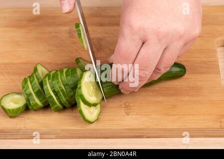 Cutting a cucumber with a knife on a cutting board. A woman cuts a cucumber with a knife. Stock Photo
