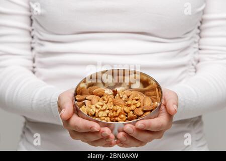 Allergy, healthy food, snack. Close up of woman hands with almond and bowl of mixed nuts, selective focus. Stock Photo