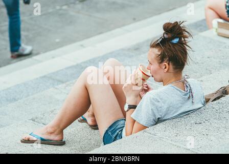Moscow, Russia - JUNE 1, 2014: A young woman is sitting on the steps of the embankment in the Park and drinking coffee. She is wearing shorts, flip Stock Photo