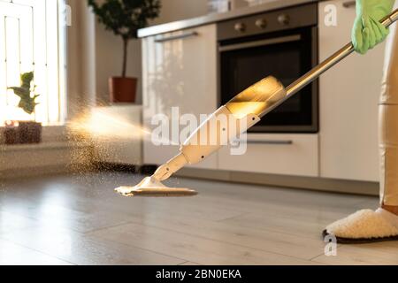 Woman in rubber gloves using microfiber spray mop pad and refillable bottle with cleaning solution, mopping the floor in apartment, doing homework cle Stock Photo