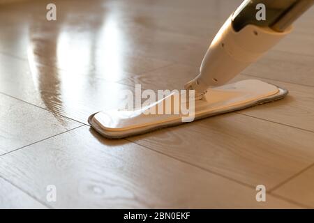 Person using spray mop pad and refillable bottle with cleaning solution, mopping the floor in apartment, doing homework cleaning routine. Close up. Ho Stock Photo