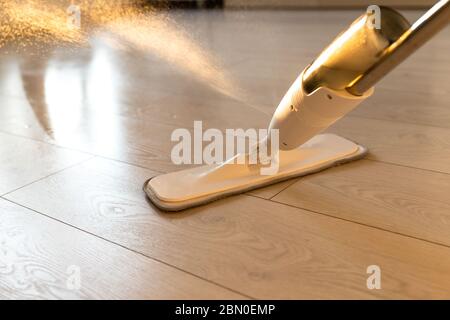 Person using spray mop pad and refillable bottle with cleaning solution, mopping the floor in apartment, doing homework cleaning routine. Close up. Ho Stock Photo