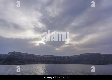 Santorini, Greece: Early morning sunshine breaks through the clouds to shine on buildings on the rim of the Santorini caldera. Stock Photo