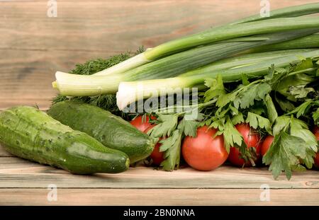 Green onions, parsley, dill, tomatoes and cucumbers on a wooden table. Greens and vegetables on a wooden table. Rustic style. Stock Photo