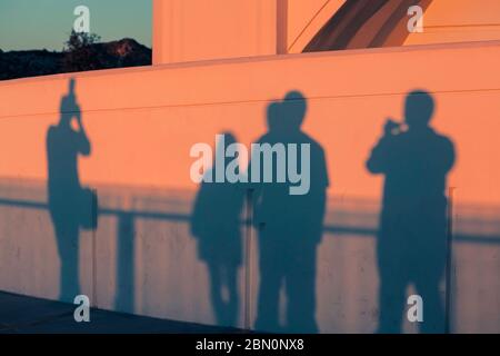 Visitors cast shadows on the wall of Griffith Park Observatory at sunset while viewing the Los Angeles skyline, California, United States, color