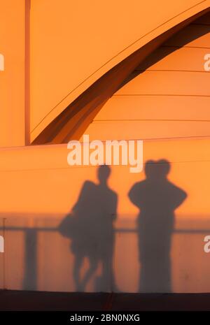 Visitors cast shadows on the wall of Griffith Park Observatory at sunset while viewing the Los Angeles skyline, California, United States, color Stock Photo