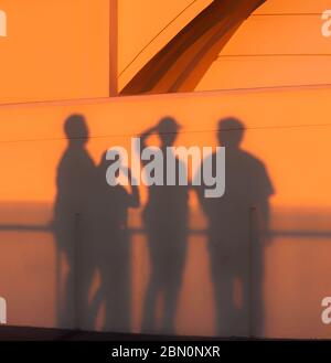 Visitors cast shadows on the wall of Griffith Park Observatory at sunset while viewing the Los Angeles skyline, California, United States, color Stock Photo