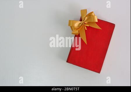 High angle view of vintage hardcover red book with golden bow placed on white table Stock Photo