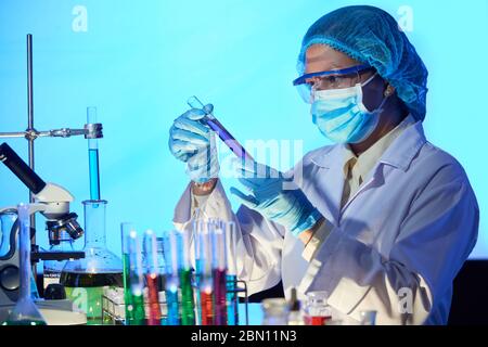 Serious Asian female researcher wearing medical mask when working with various reagents in laboratory Stock Photo