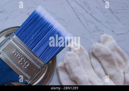 A blue brush lies on top of the can. Against the background of a cement floor. Protective gloves. View from above. Selective focus. Copyspace Stock Photo