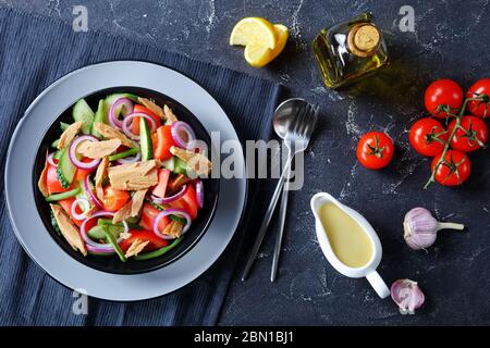 Mediterranean salad of green bean, cucumber and canned tuna with tomatoes and red onion rings on a black plate on a dark concrete background with oliv Stock Photo