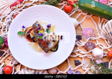 White fish and vegetables, italian recipe, served in a black plate on a seaside theme background Stock Photo