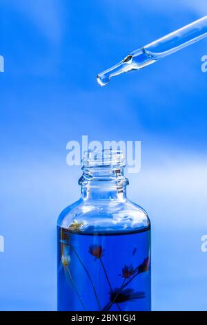 Dropper glass Bottle Mock-Up. Oily drop falls from cosmetic pipette on blue background. Color of the year, Stock Photo