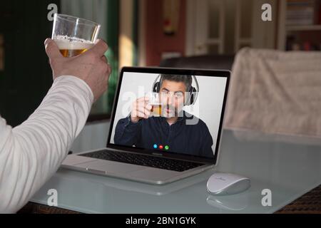 Person sharing a glass of beer with his friend through a technology platform during quarantine isolation Stock Photo