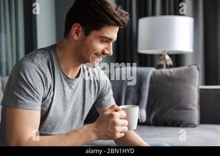 Image of a handsome cheerful young man indoors at home drinking coffee. Stock Photo