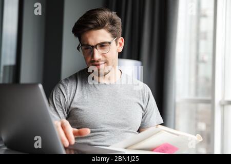 Handsome serious young bearded man wearing casual clothes using laptop computer while sitting at the table at home Stock Photo
