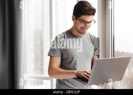 Image of a positive optimistic young man indoors at home using laptop computer. Stock Photo
