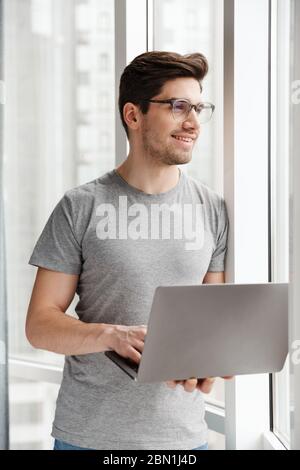 Image of a positive optimistic young man indoors at home using laptop computer. Stock Photo