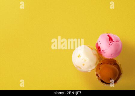 Ice cream of chocolate, vanilla, and strawberry on vivid yellow background Stock Photo