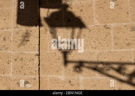 Wall of a house created from blocks with a shadow of a traditional lantern. Sunny day. Alghero, Sardinia, Italy. Stock Photo