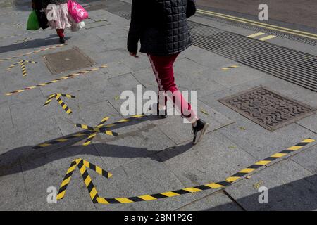 The day after UK Prime Minister Boris Johnson addressed the nation with his roadmap for the coming weeks and months during the Coronavirus pandemic lockdown, south Londoners's feet and legs pass over the now worn hazard tape that marks out safe social distancing practice at East Street Market on the Walworth Road, on 11th May 2020, in London, England. Stock Photo