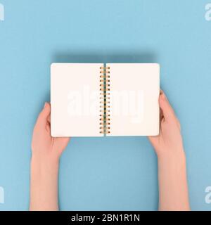 Female hands hold copybook. Blank notebook mockup on a blue pastel background. Stock Photo