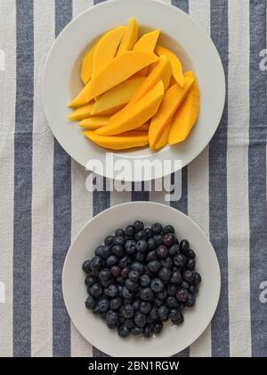 Slices of mango and blueberries on a blue and white striped tablecloth Stock Photo
