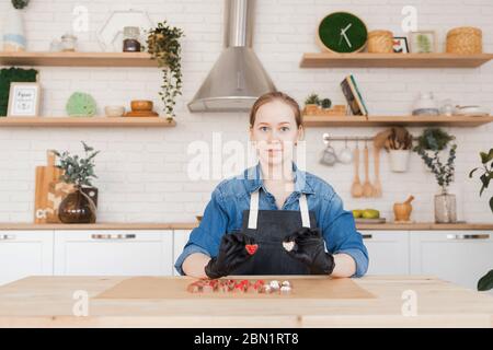 Confectioner holds sweet Belgian chocolate candies on kitchen background. Small business home concept. Stock Photo