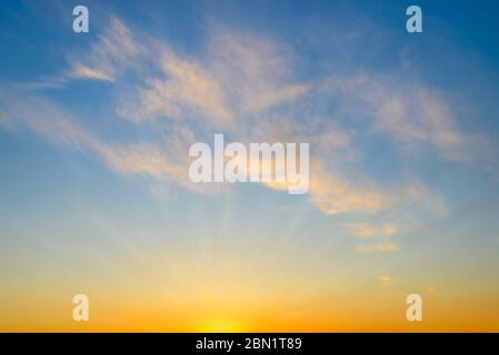 Summer sunrise sky with sunbeams and few golden translucent clouds. Beautiful dawn skyscape. Clear paradise sky at early morning. Calm blue heaven. Stock Photo