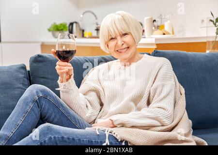 Retirement. Senior woman sitting at home drinking red wine miling cheerful and relaxed Stock Photo