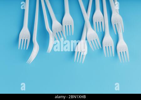 White plastic forks of disposable tableware on a blue background. Free space, top view. Stock Photo