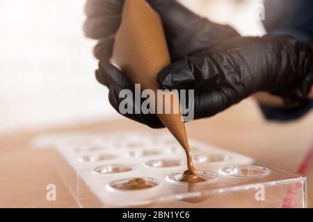 Chef or chocolatier pouring melted dark chocolate into silicone molds on pastry bag Stock Photo